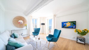 Un salon moderne comprenant un canapé, deux fauteuils bleus, une table basse, un téléviseur et une grande fenêtre donnant sur un beau paysage.