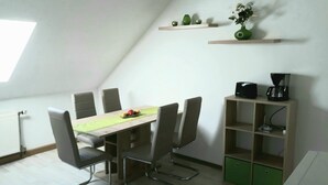 A dining area with a table, chairs, a coffee machine, and a shelf with decorative items. - Large 90 sqm vacation apartment (Schönstedt)