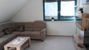 A living room with a brown sectional sofa, a wooden coffee table, and a small potted plant on the windowsill. - Large 90 sqm vacation apartment (Schönstedt)
