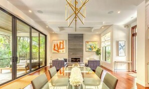 A modern dining room with a glass table, grey sofas, and a fireplace.