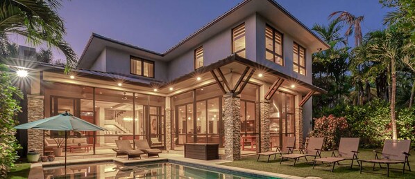 Ein modernes Haus mit Swimmingpool, Sitzgelegenheiten im Freien und einem gut beleuchteten Innenraum.