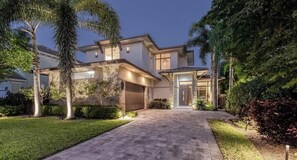 A modern house with a paved driveway, stone pillars, and a well-maintained lawn.