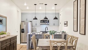 A modern kitchen with white cabinets, stainless steel appliances, and a wooden dining table with chairs. - Desert Color's Sunshine and Sage: Lagoon + Beaches (St. George)