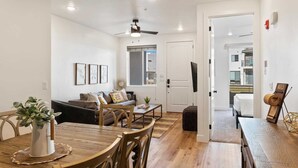 A modern living room with a wooden dining table, a sofa, and a ceiling fan. - Desert Color's Sunshine and Sage: Lagoon + Beaches (St. George)