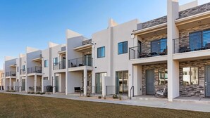 A row of modern multi-story residential buildings with balconies, large windows, and a well-maintained lawn. - Desert Color's Sunshine and Sage: Lagoon + Beaches (St. George)
