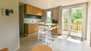A modern kitchen with a bar area, large windows, and a view of the outdoors. - Domaine Les Rousselieres (Les Sables-d'Olonne)