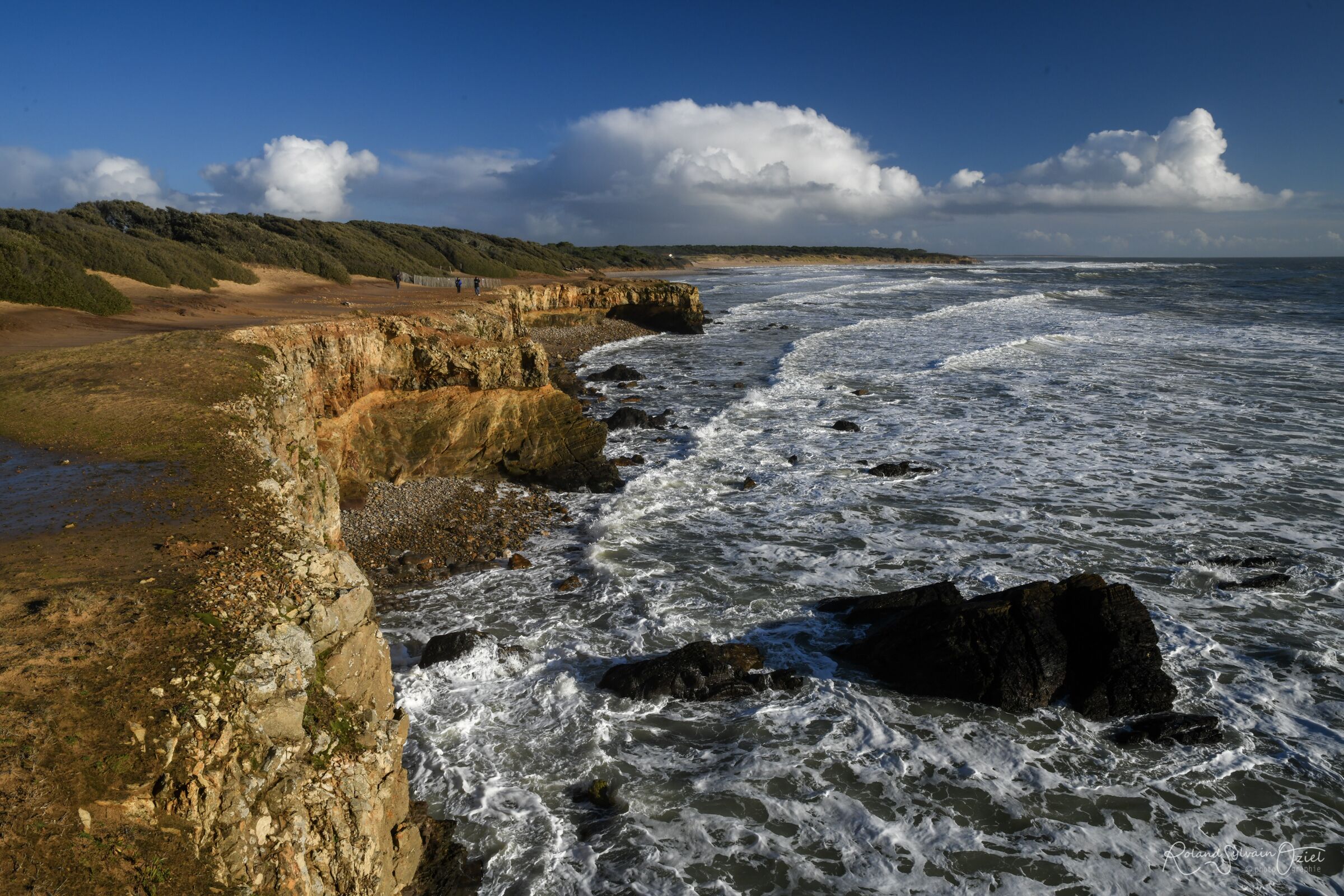A coastal landscape with rocky cliffs, a sandy beach, and the ocean.
