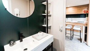 A modern bathroom with a white vanity, a round mirror, and a dark green accent wall. - Domaine Les Rousselieres (Les Sables-d'Olonne)