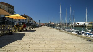 A paved waterfront promenade with outdoor seating, a row of boats docked on the right, and buildings along the left side. - Domaine Les Rousselieres (Les Sables-d'Olonne)