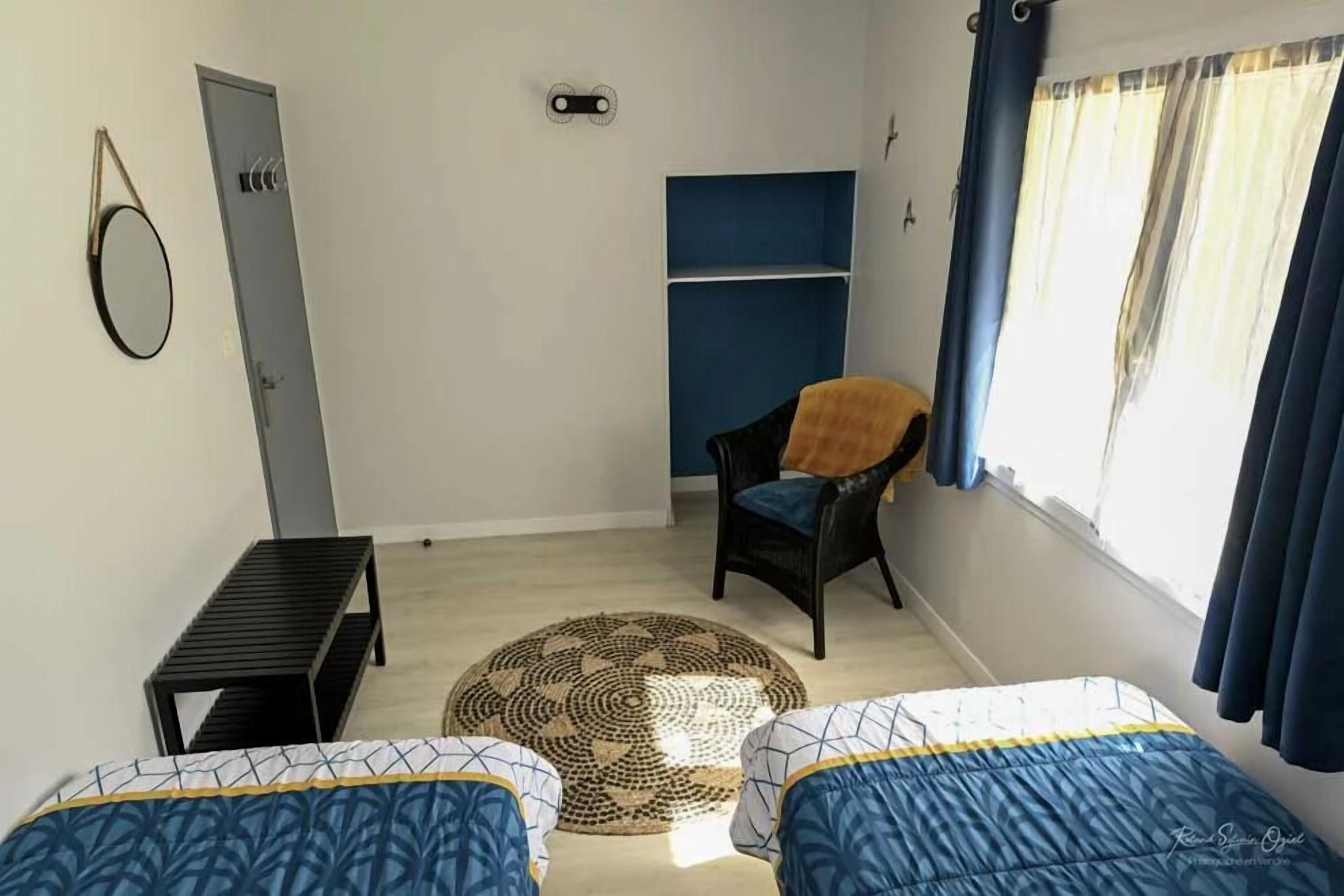 Une pièce avec deux lits, une chaise, une petite table, une porte et une fenêtre avec des rideaux.