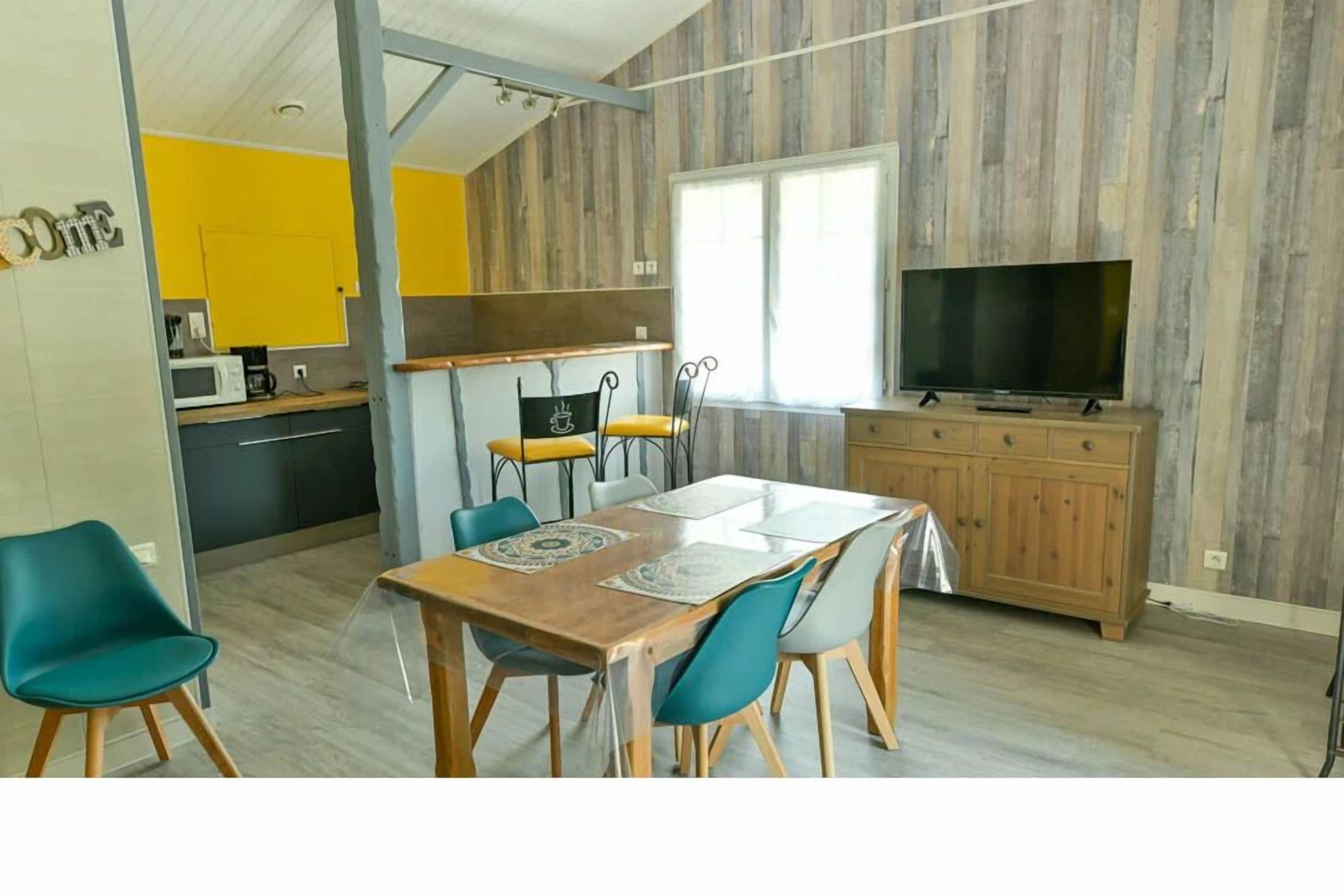 A dining area with a wooden table, teal chairs, and a TV on a wooden cabinet.