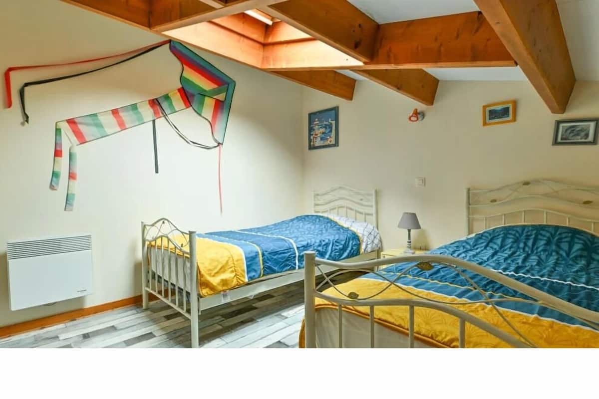 A bedroom with two beds, wooden beams, a radiator, and a skylight.