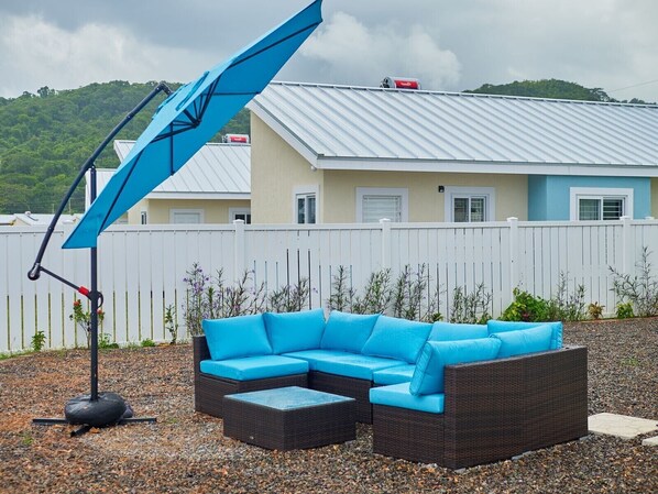 A blue sectional sofa with a matching ottoman, a blue umbrella, and a gravel patio area.