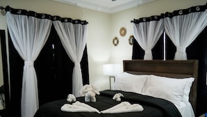 Ein Hotelzimmer mit einem großen Bett, schwarz-weißen Vorhängen, einem Holz-Kopfteil und einem Nachttisch mit Lampe.
