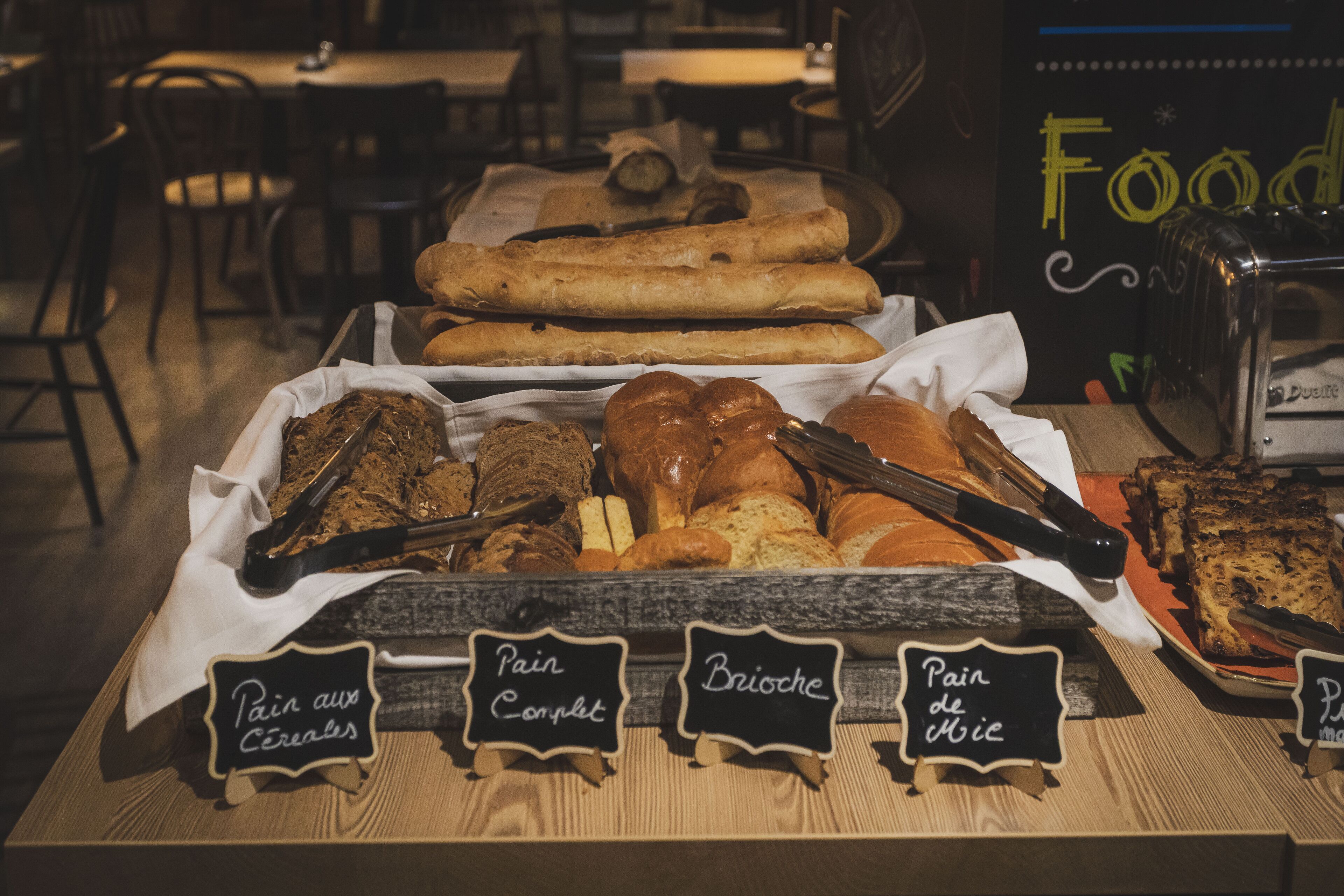 A bakery display with various breads and pastries, including labels for 'Pain aux Céréales' and 'Pain Complet'.