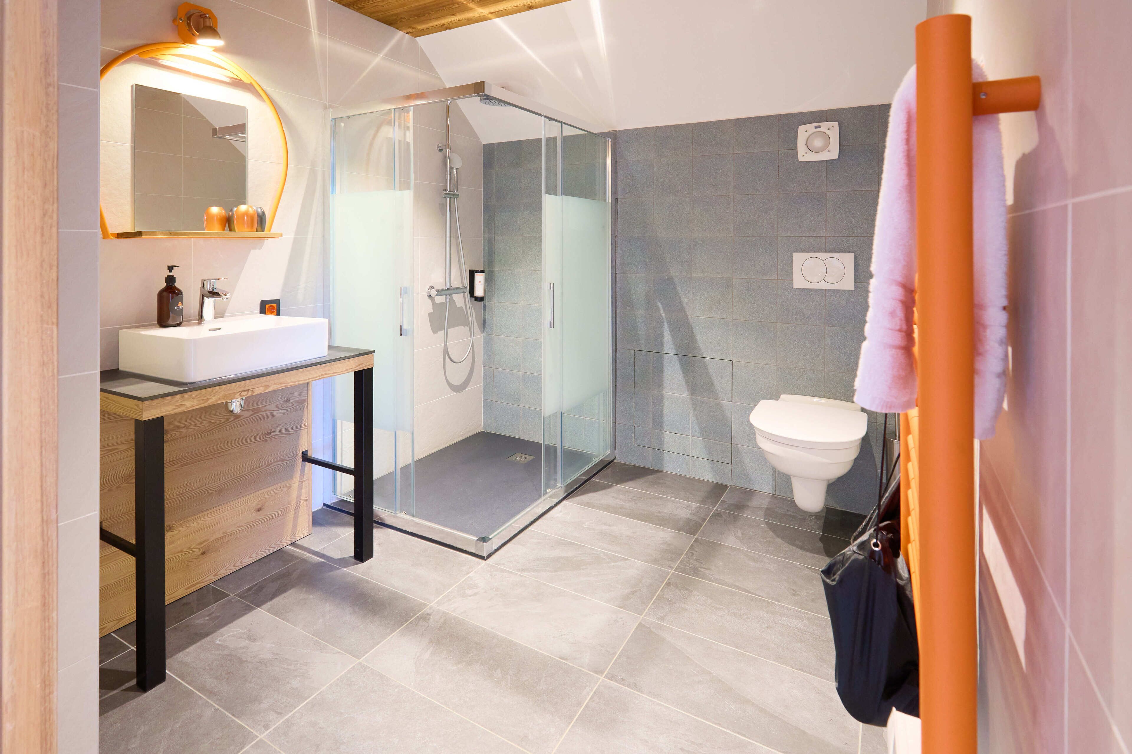 Une salle de bain moderne avec une douche à parois de verre, un meuble-lavabo en bois avec un miroir et des toilettes blanches.