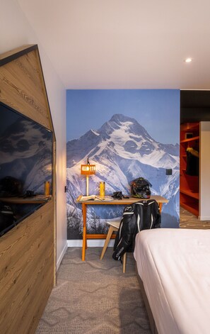 A hotel room with a mountain mural, a desk with a lamp, a bed, and a backpack. - Base Camp Lodge Les 2 Alpes  (Les Deux Alpes)