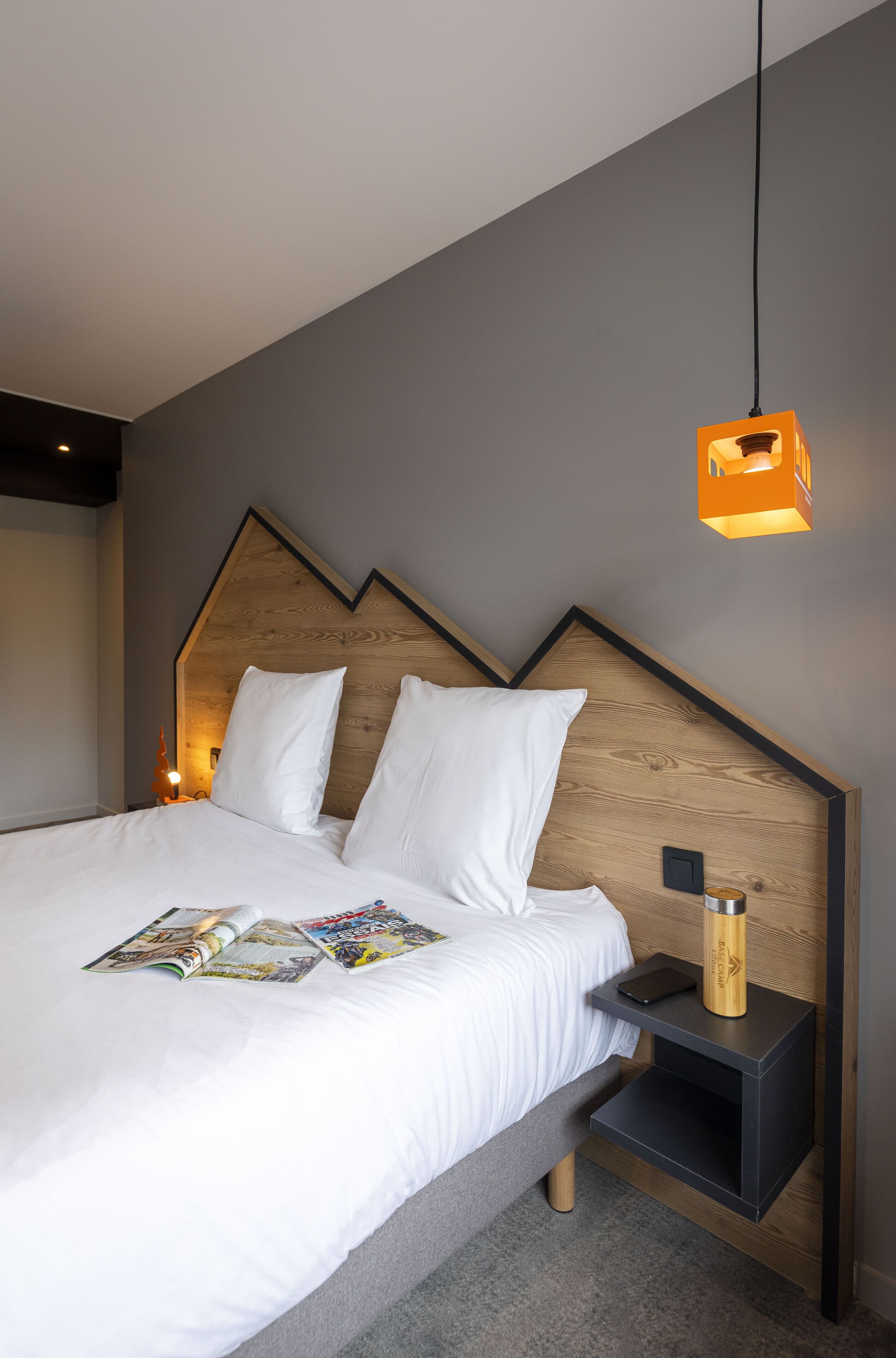 Une chambre à coucher moderne avec une tête de lit en bois, une table de chevet avec une lampe et un magazine sur le lit.