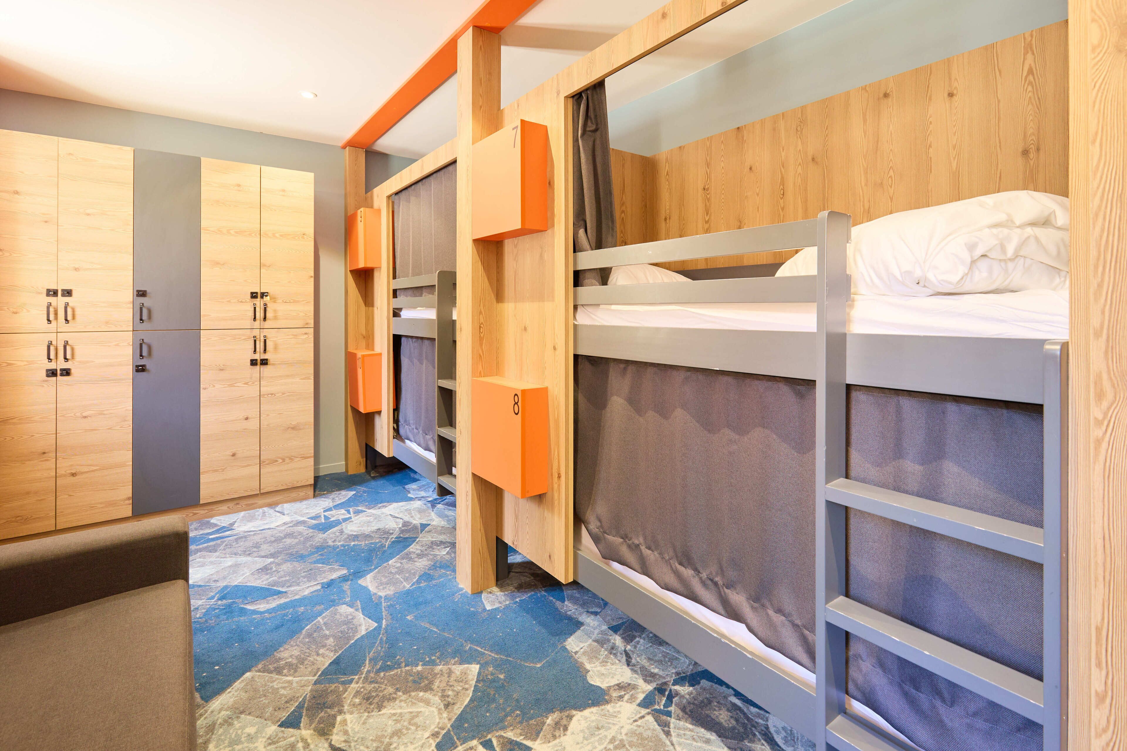 A bunk room with wooden bunk beds, a wardrobe with a grey door, and a patterned floor.