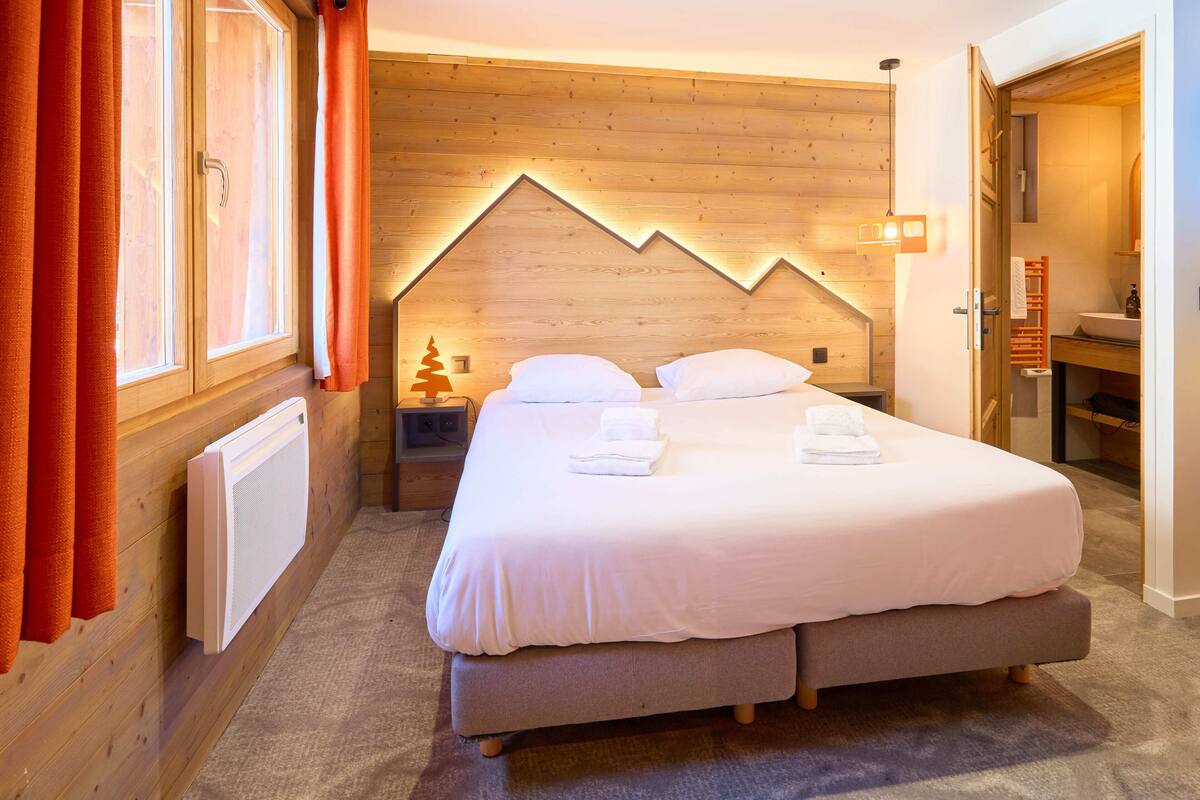 Une chambre à coucher avec un grand lit, une tête de lit en bois et une fenêtre avec des rideaux.