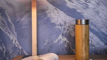 A room with a mountain-themed wall, a wooden table with a magazine, a lamp, and a stainless steel thermos.