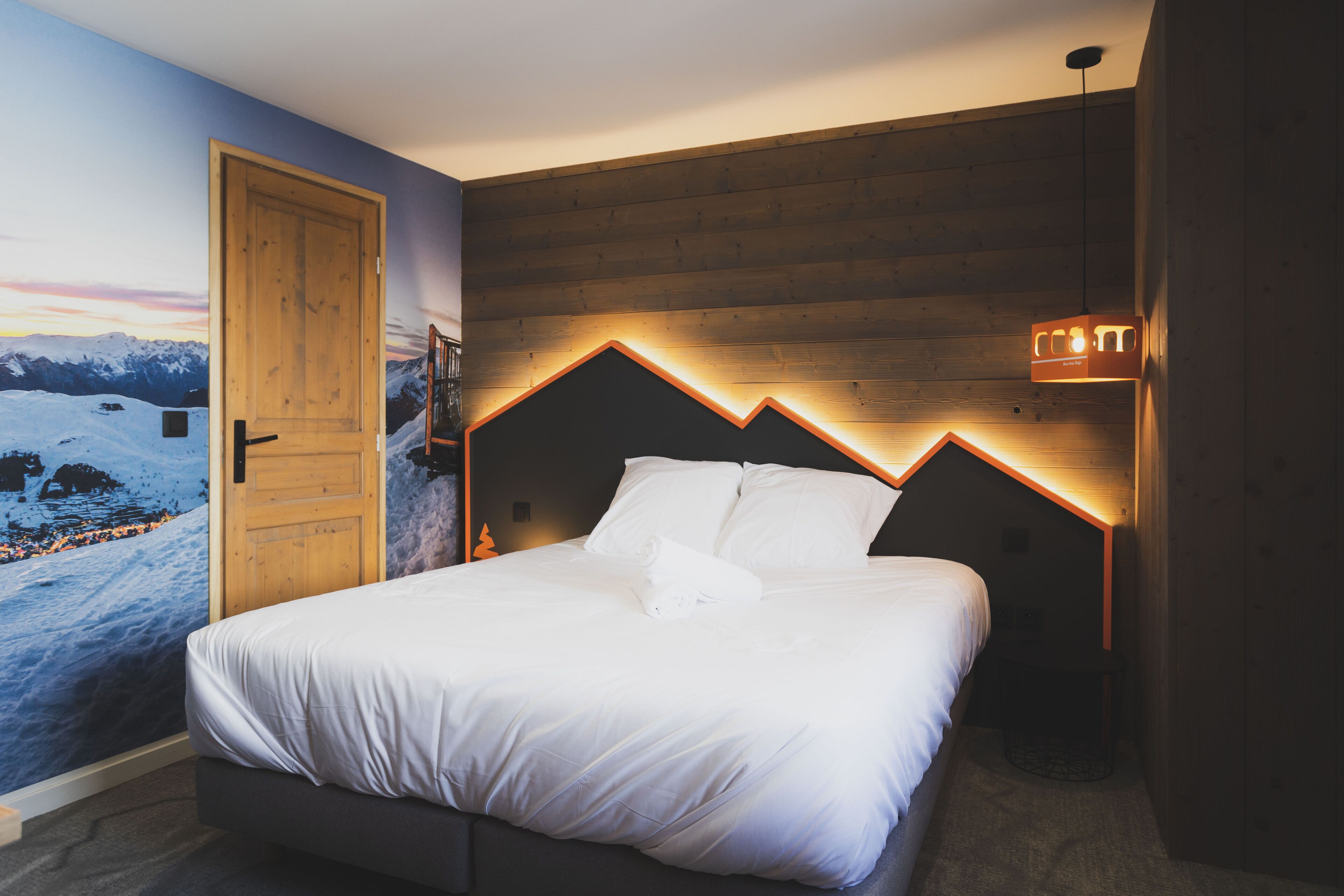 A bedroom with a wooden headboard, a bed with white bedding, a nightstand, and a wall-mounted light fixture.