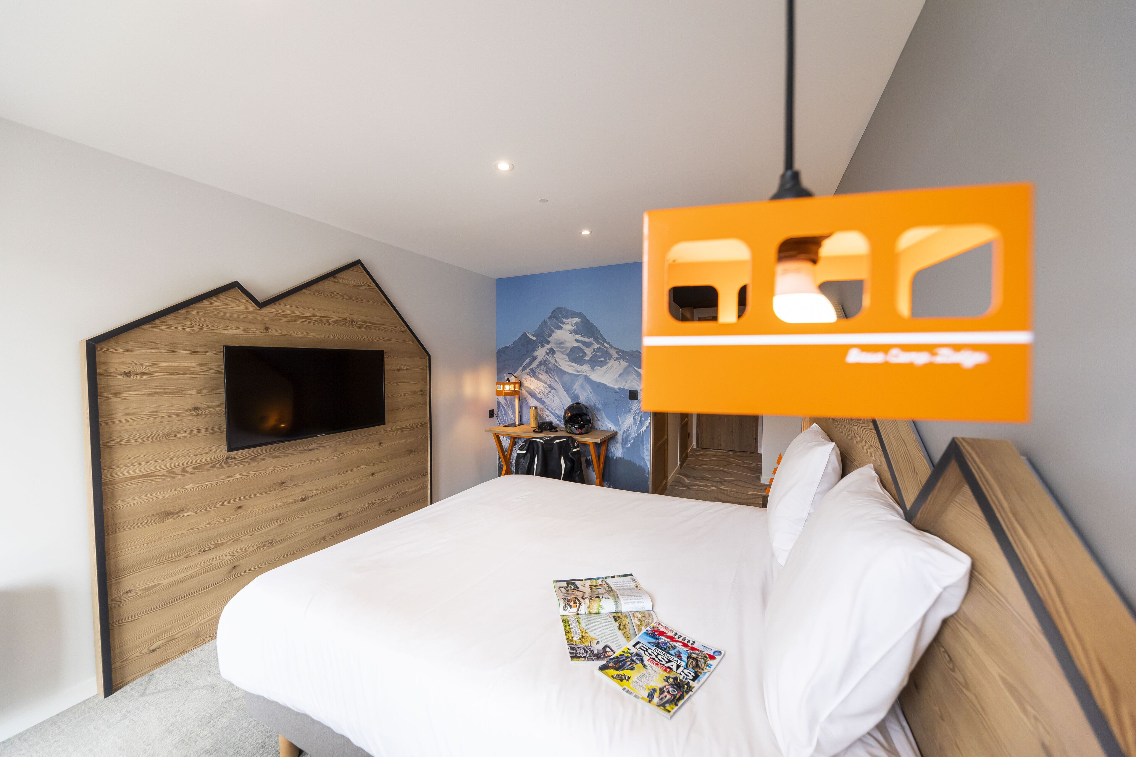 A hotel room with a bed, a wooden headboard, a mountain mural, and a hanging orange sign.