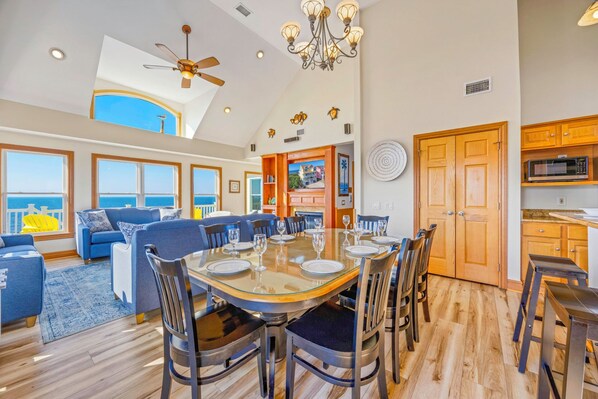 A spacious dining area with a high ceiling, large windows, and a view of the ocean.
