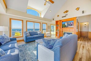 A spacious living room with a large window, a fireplace, and a view of the ocean.