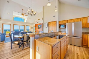 A spacious kitchen with wooden cabinets, a stainless steel refrigerator, and a dining area with a view of the ocean.