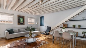 A modern living room with a sofa, a coffee table, and a dining area with chairs and a table. - Waou Puerta del Sol II - Alquiler Corta Duración (Madrid)