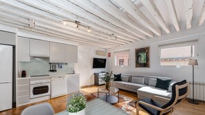 A modern kitchen with white cabinets, a built-in oven, and a dining area with a glass table and a potted plant. - Waou Puerta del Sol II - Alquiler Corta Duración (Madrid)