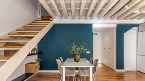 A modern interior with a staircase, a dining table with chairs, and a vase with flowers. - Waou Puerta del Sol II - Alquiler Corta Duración (Madrid)