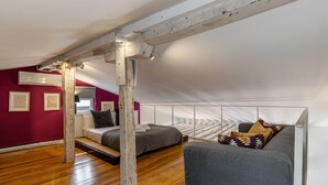 A loft-style room with exposed wooden beams, a red accent wall, and a large window. - Waou Puerta del Sol II - Alquiler Corta Duración (Madrid)