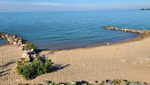 A sandy beach with a rocky breakwater and calm blue water.