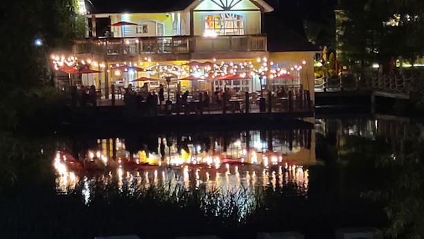 A waterfront building with outdoor seating and a reflection in the water.