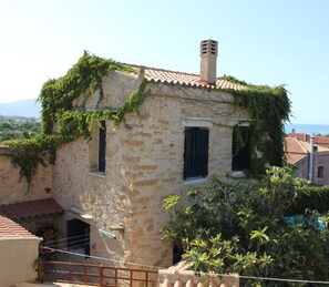 A stone building with ivy-covered walls, a chimney, and a view of the sea.