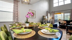 Un coin repas avec une table ronde dressée pour quatre personnes, entourée de chaises recouvertes d’un tissu vert.