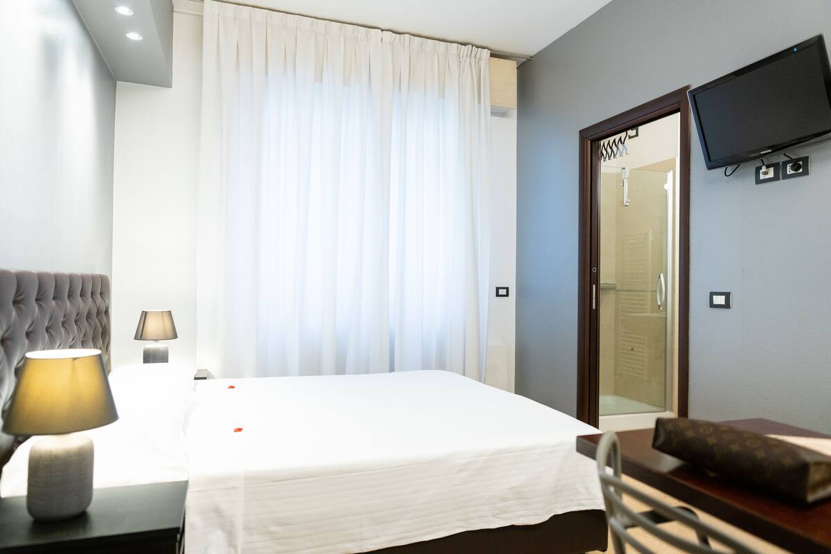 A hotel room with a bed, a bedside lamp, a flat-screen TV, and a mirror.