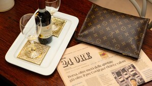 A dining table with a bottle of wine, glasses, a wallet, and a newspaper.