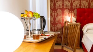 A breakfast tray with fruits, a glass of juice, and a coffee pot on a wooden table in a room with a red patterned wall and a red bed.