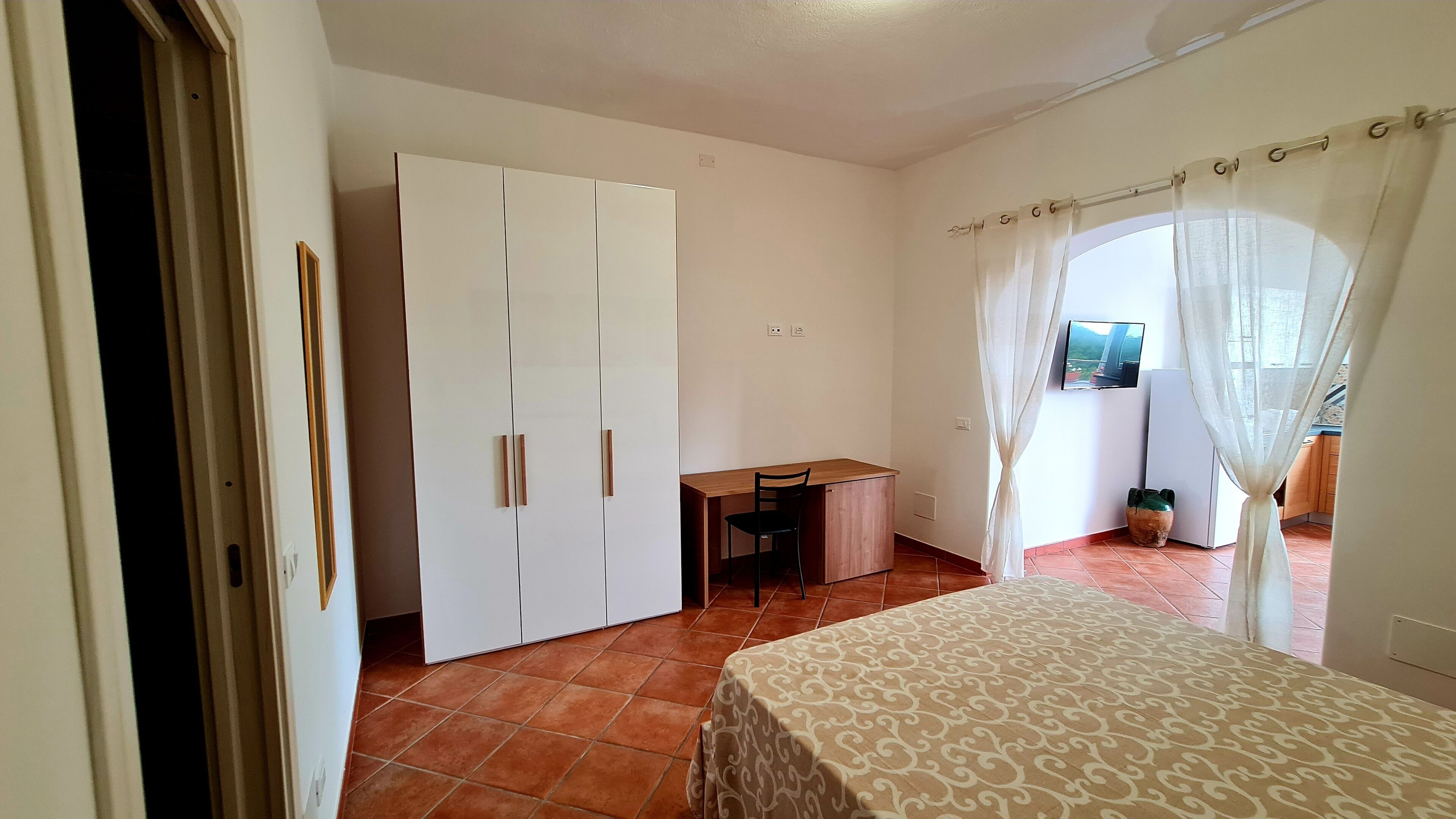 A bedroom with a bed, a desk, and a wardrobe.