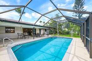 Une piscine entourée de parois en verre, des meubles d’extérieur et une vue sur des palmiers.