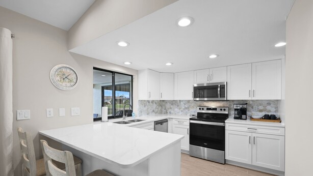 A modern kitchen with white cabinetry, a central island, stainless steel appliances, and a view through the glass door. - Look at this View with direct Gulf Access (Cape Coral)