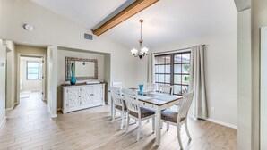 A dining area with a wooden table and chairs, a chandelier, and a large window with curtains. - Look at this View with direct Gulf Access (Cape Coral)
