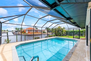 En swimmingpool med udsigt over en kanal og et hus på den anden side af vandet.