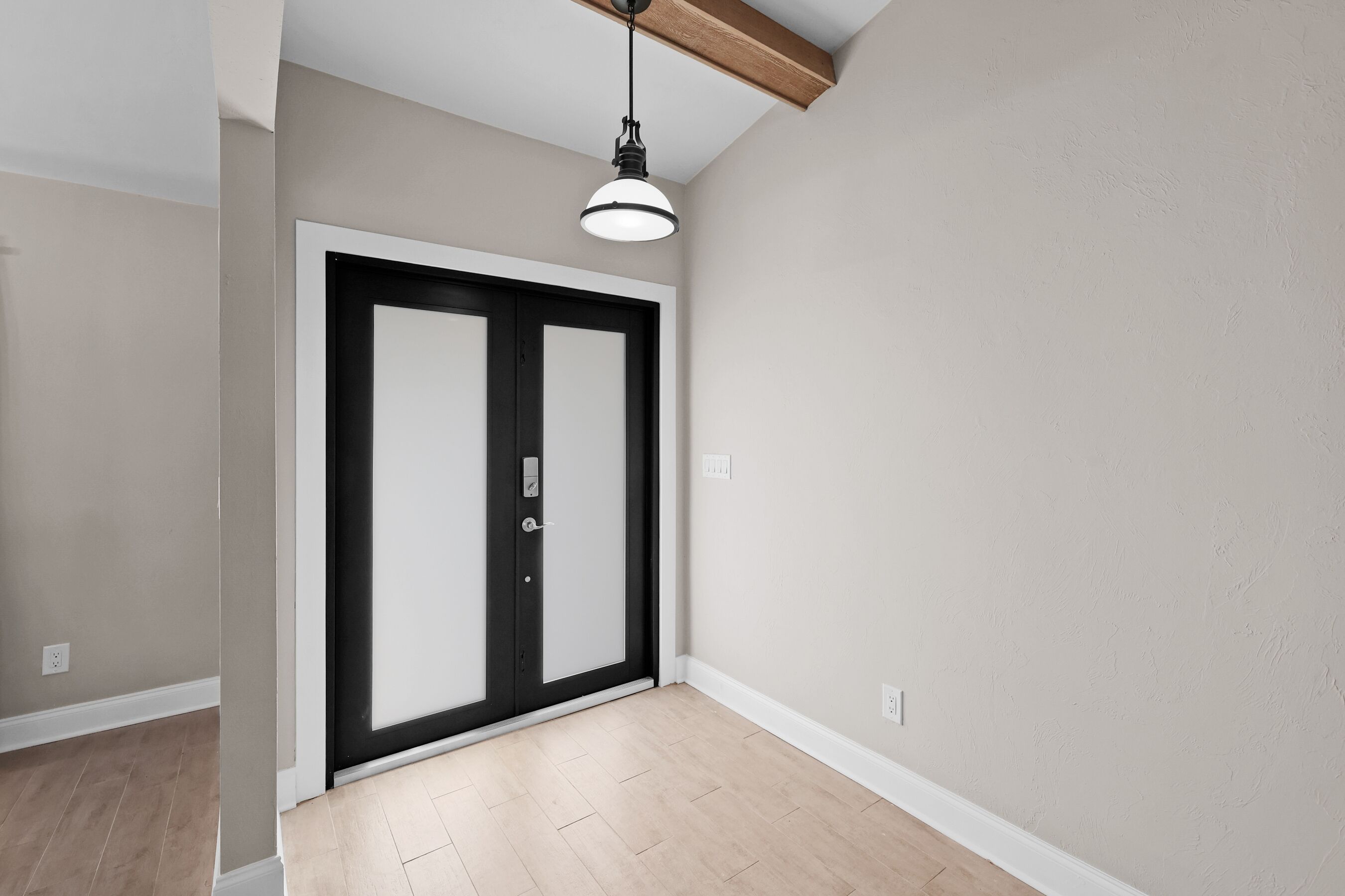 A hallway with a double door, a ceiling light fixture, and a light-colored wooden floor.