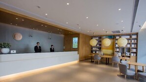 A modern reception area with a reception desk, two staff members, a large screen, and a seating area with tables and chairs. - Ji Hotel (Shanghai)