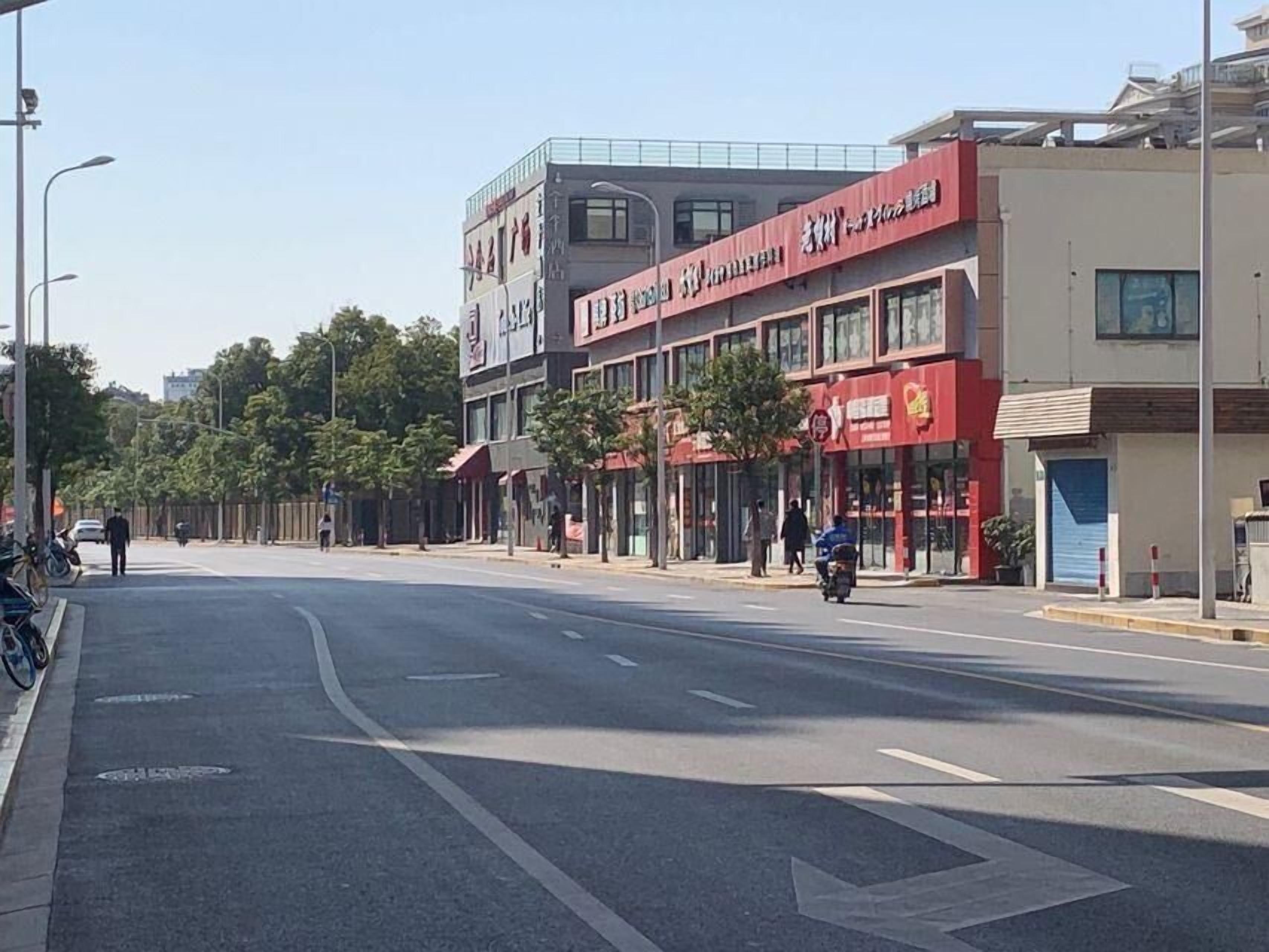 Une vue de rue avec des bâtiments, un ciel dégagé et quelques piétons.