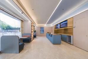 A modern reception area with a counter, seating, and a view through a glass wall. - Ji Hotel (Shanghai)